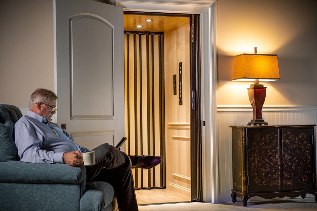 A man sitting in a chair next to a residential elevator.